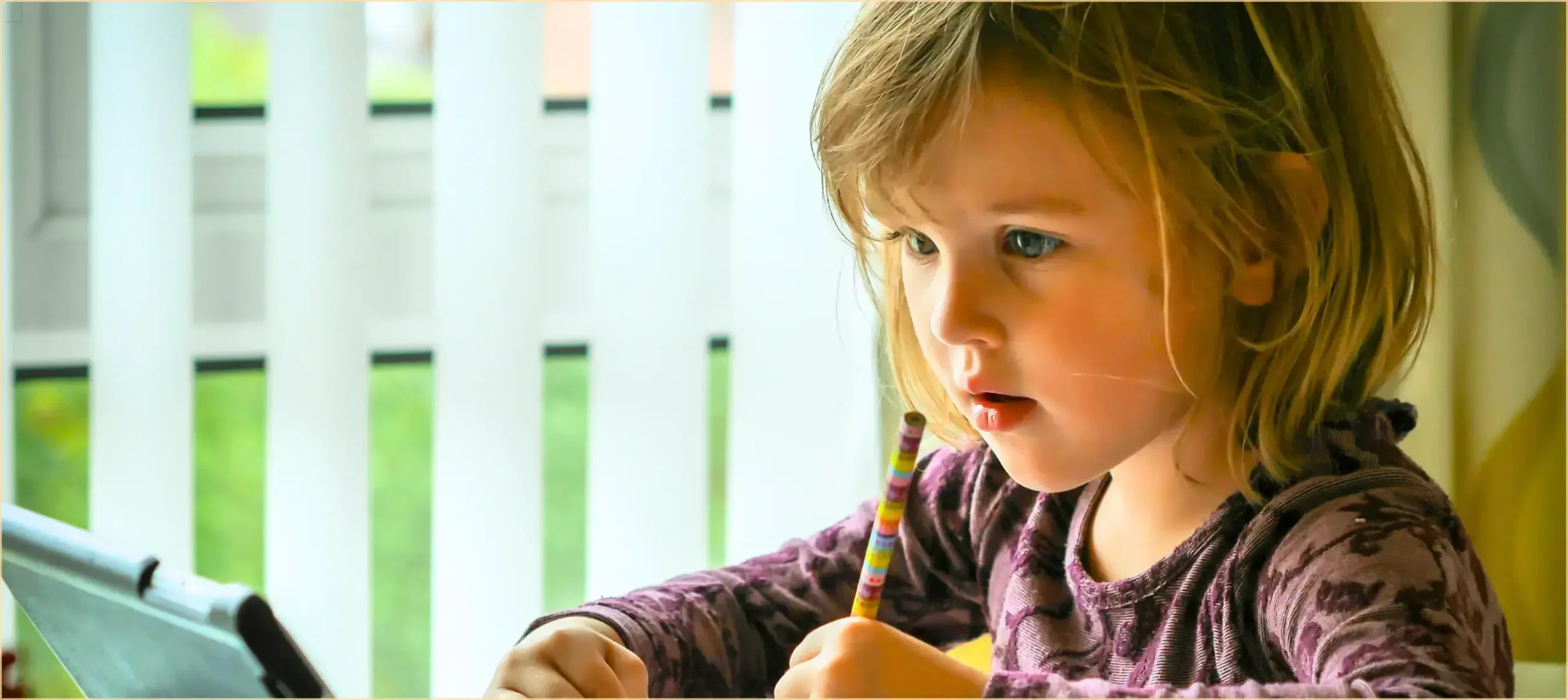 Kleines Mädchen sitzt am Tablett und schreibt etwas auf