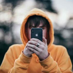 Pubertät bei Jungen Junge blickt auf hochgehaltenes Smartphone der Marke Apple