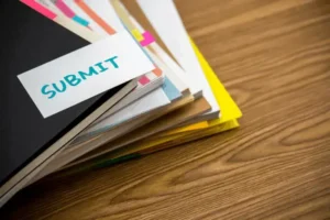 Ein kleiner Haufen Papiere und Hefte mit einer Notiz oben drauf, die sagt "submit" (eng: einreichen)