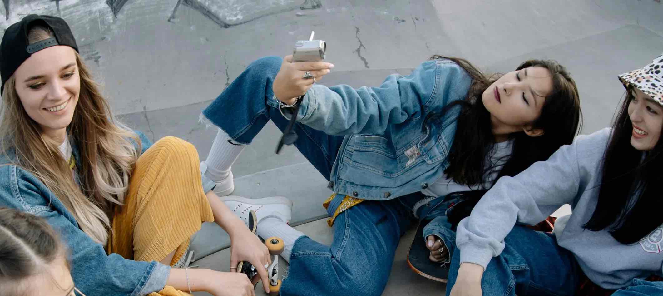 Teenager sitzen auf einem Skatepark; ein Mädchen macht ein Selfie mit ihrer Freundin